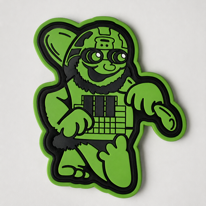 A green and black cartoon character patch or sticker shown on a plain light background. The character has a beard, large glasses, and is holding a keyboard.