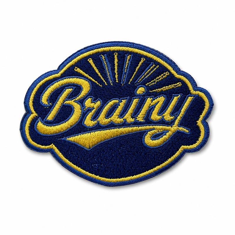 An embroidered oval patch with the word 'Brainy' in yellow cursive script over a dark blue background, with yellow rays and a yellow border.